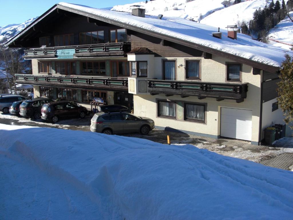 a large building with cars parked in the snow at Hotel-Pension Flora in Saalbach Hinterglemm