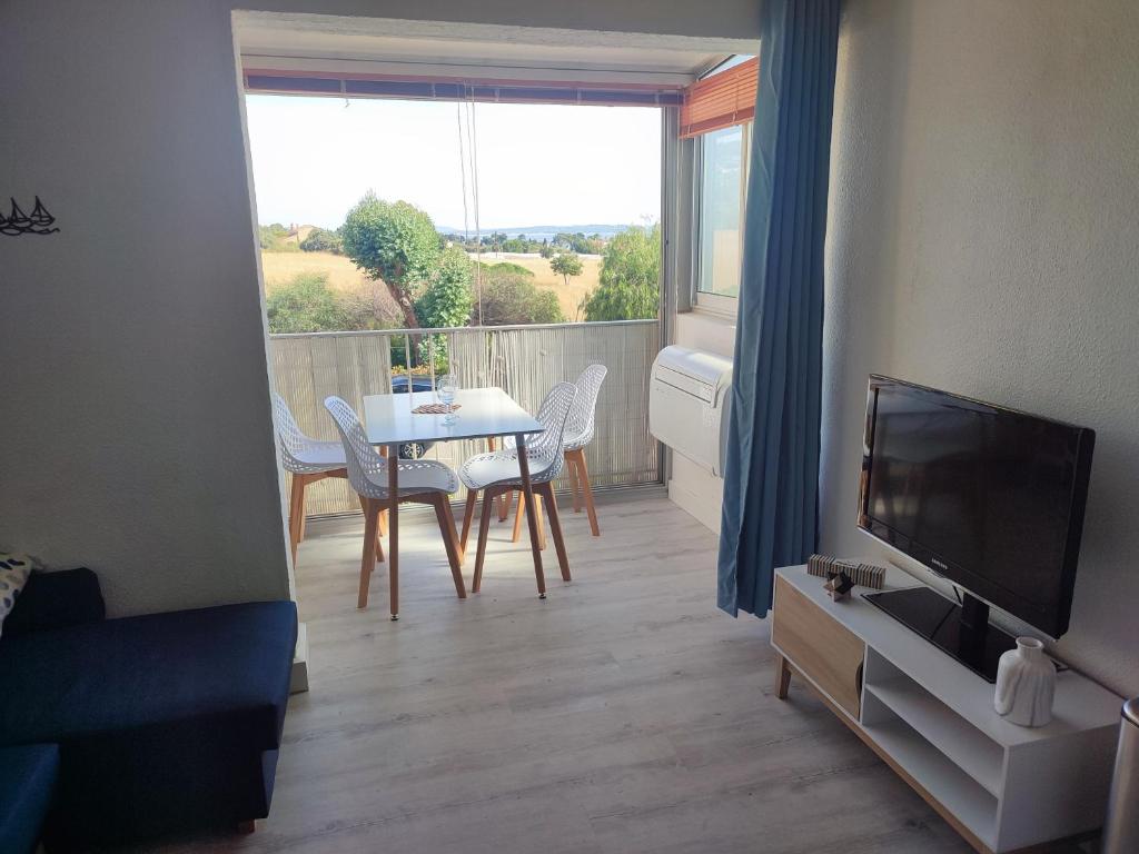 un salon avec une télévision et une table avec des chaises dans l'établissement Agréable appartement avec vue mer, à Carqueiranne
