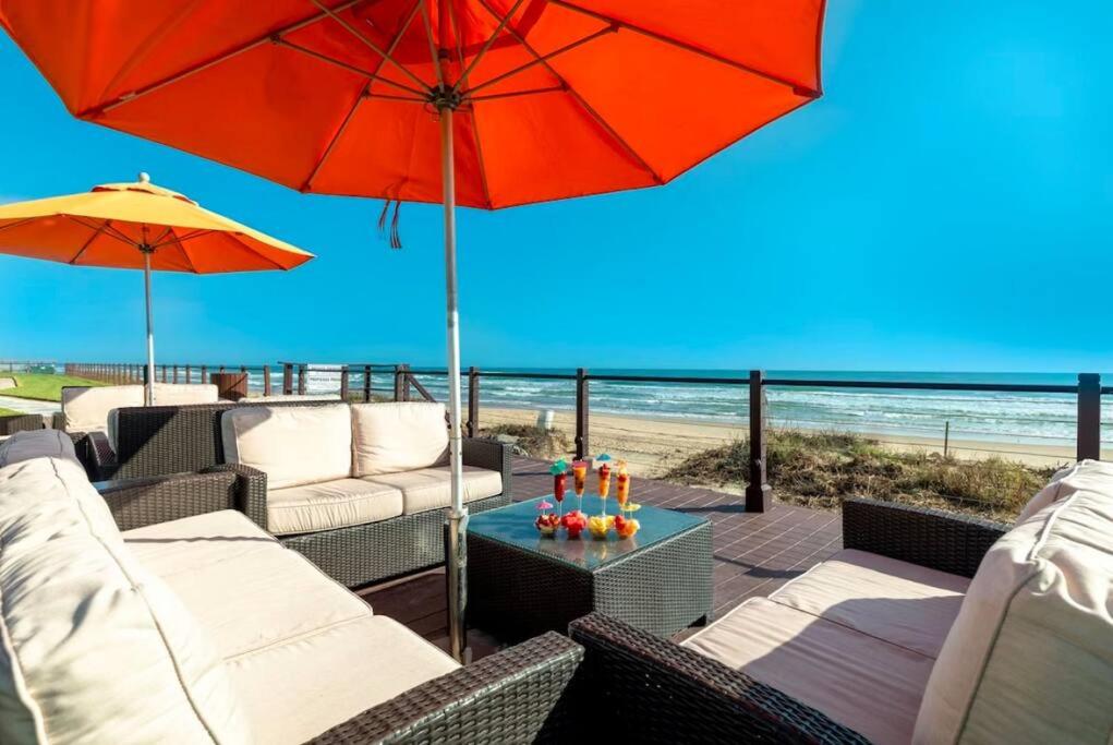 eine Terrasse mit Stühlen, Sonnenschirm und Strand in der Unterkunft Beachfront Resort 2BR Condo 3 Pools, Heated Pool, Kids Pool & Jacuzzi in South Padre Island