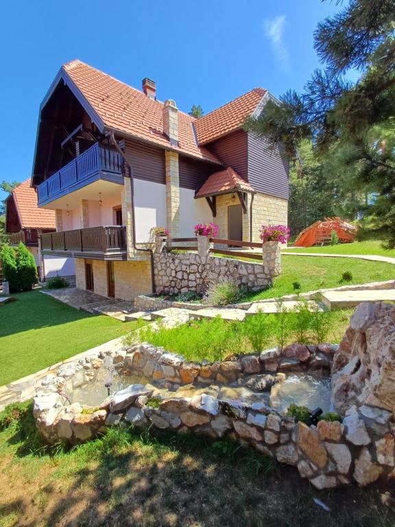 a house with a stone retaining wall and a pond at Tara Apartmani Malešević - 2 in Bajina Bašta