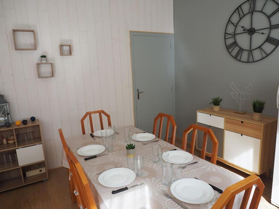 une table à manger avec des assiettes, des chaises et une horloge dans l'établissement Appartement Mont-dore centre 6-8 personnes 2 ch, à Le Mont-Dore