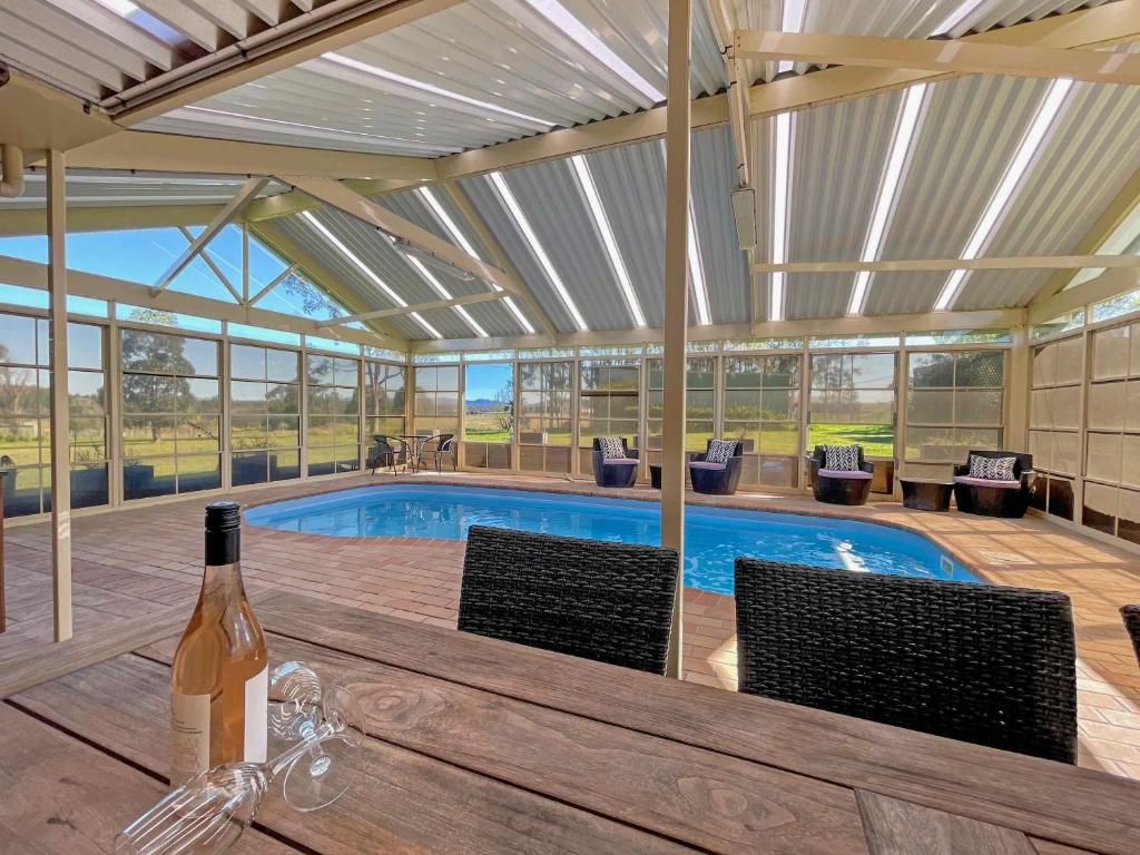 a bottle of wine sitting on a table next to a swimming pool at Nottage Cottage in Branxton