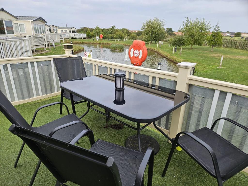 a table and chairs on a balcony with a view of a river at Buckley's Retreat - 3 Bedroom Family Caravan overlooking fishing lakes at Golden Palm Resort in Chapel Saint Leonards