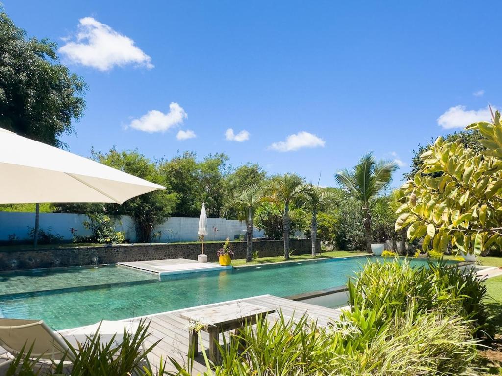 a swimming pool with an umbrella and chairs and trees at Domaine Putu Bali - Havre de paix & Piscine Lagon in Petit Raffray