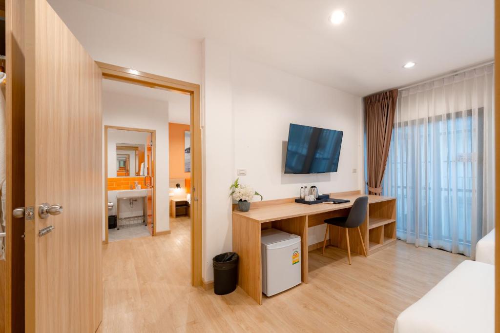 A room with a long desk, television, minibar and curtained window beside the bed.
