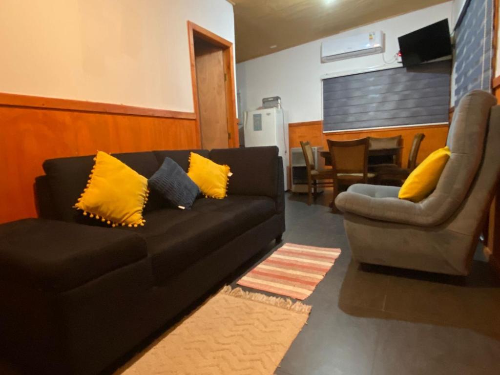 a living room with a black couch and a chair at Cabaña muy cómoda cerca de Saltos del Laja in Cabrero