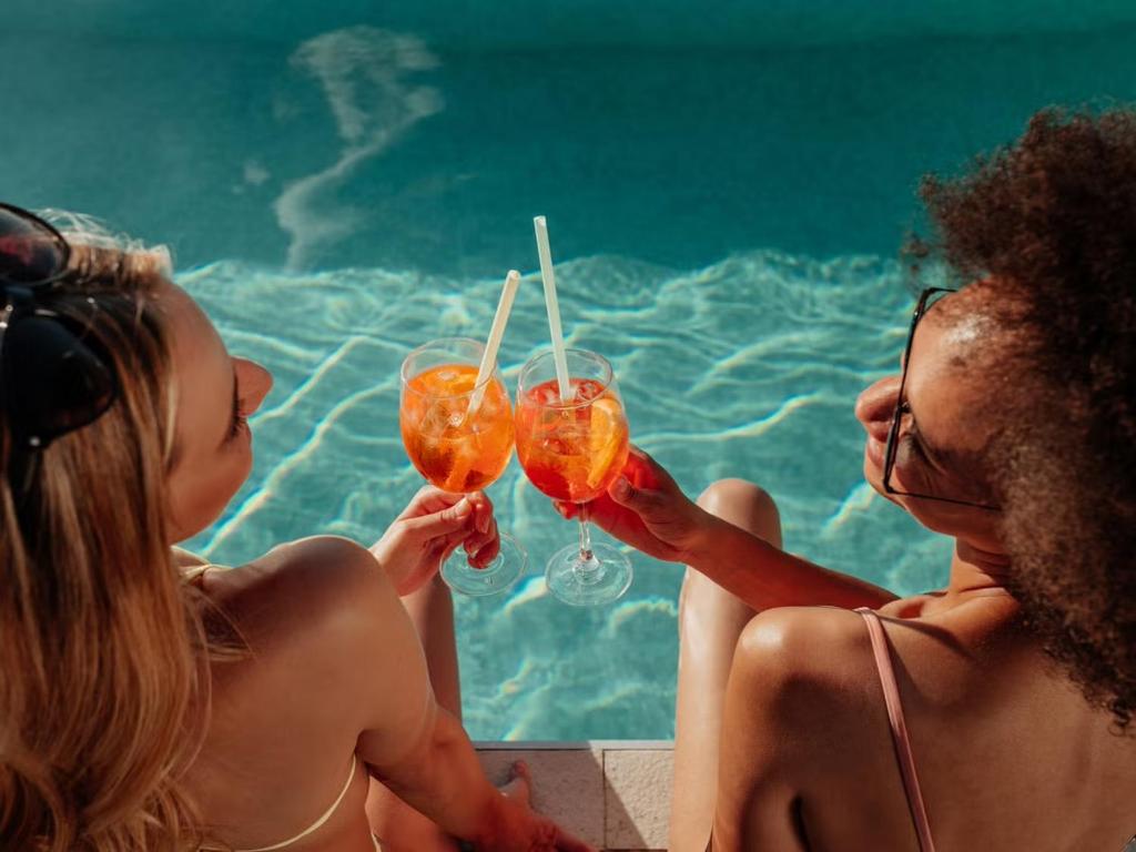 two women sitting next to a swimming pool holding drinks at WakakaPackers in Kuala Lumpur
