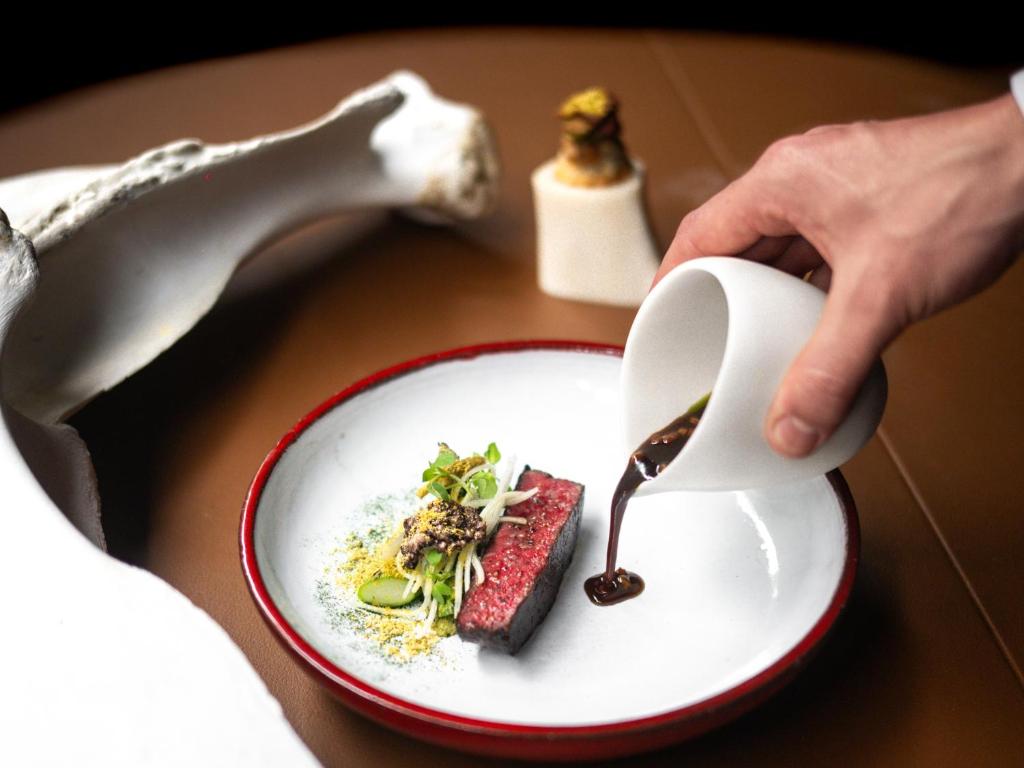 a person holding a white plate with food on a table at MUNI KYOTO by Onko Chishin in Kyoto