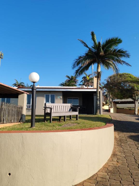 a park bench in front of a house with a palm tree at Chakas Rock Chalets - Unit 19 in Ballito