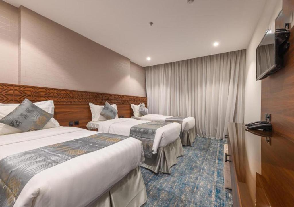 a hotel room with three beds and a television at Manazel Al Zaireen Hotel in Makkah