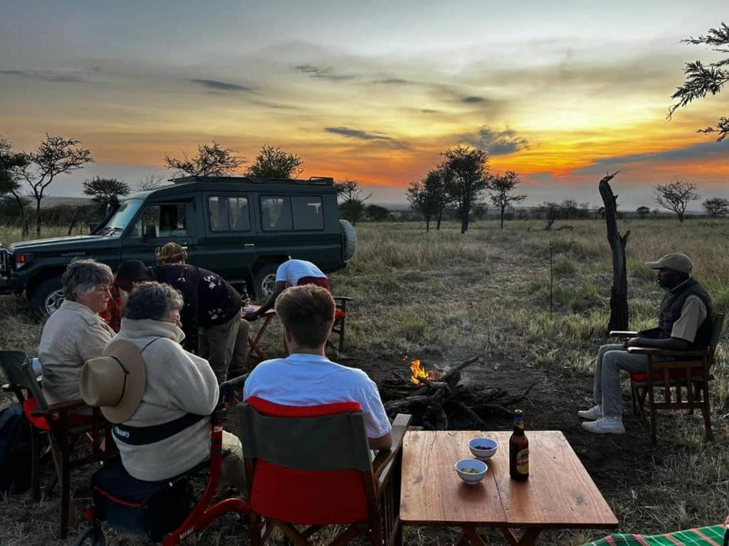 a group of people sitting around a fire in front of a truck at Sadanga & Sons Mobile Camp Safaris in Mugumu