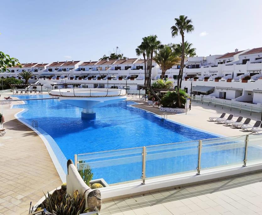 a large swimming pool in a resort with chairs and buildings at Amantes del Mar, Heated pool in Costa Del Silencio