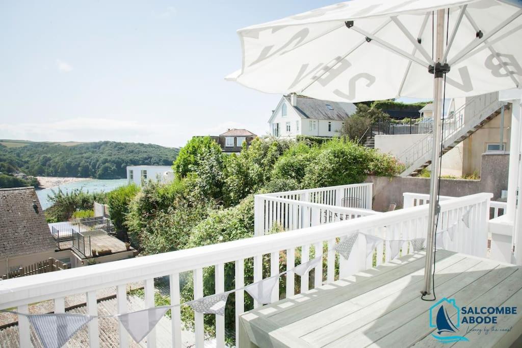 a balcony with an umbrella and a view of the water at Beach View - Stylish Stay, Estuary Views & Luxury Spa Access in Salcombe