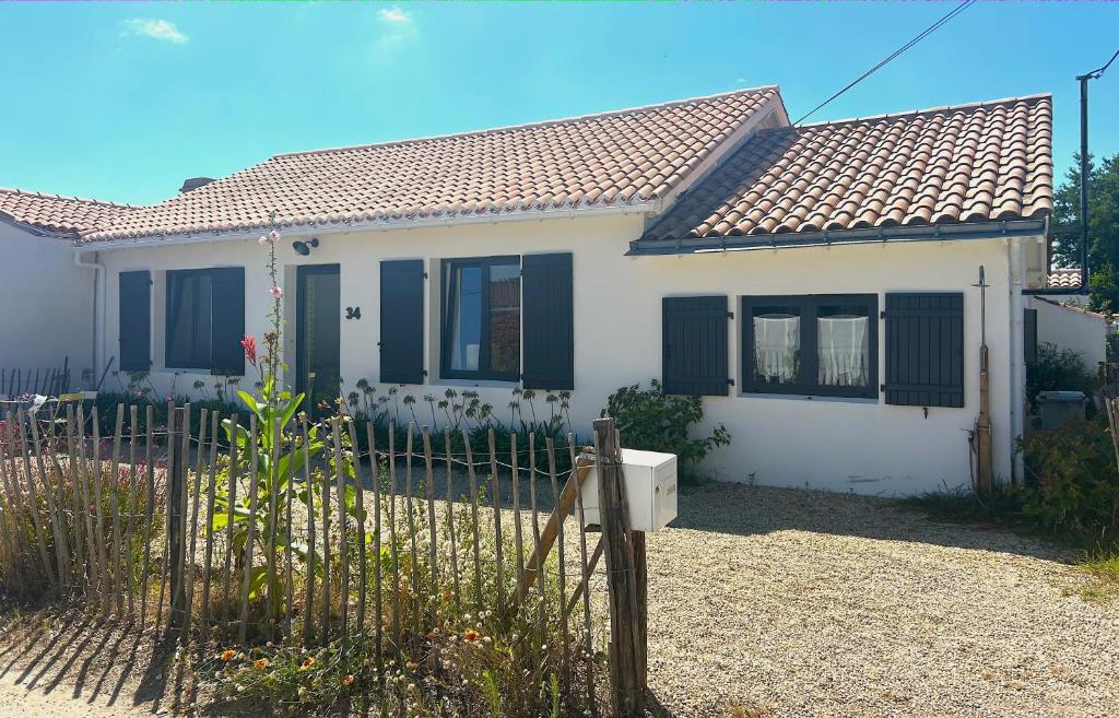ein weißes Haus mit schwarzen Fenstern und einem Zaun in der Unterkunft Maison 8 personnes à 100 m de la plage de la Clère in Le Grand Vieil