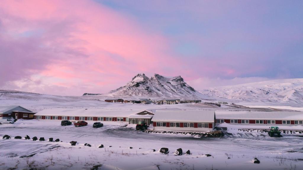 a building in the snow with a mountain in the background at Hótel Dyrhólaey in Vík