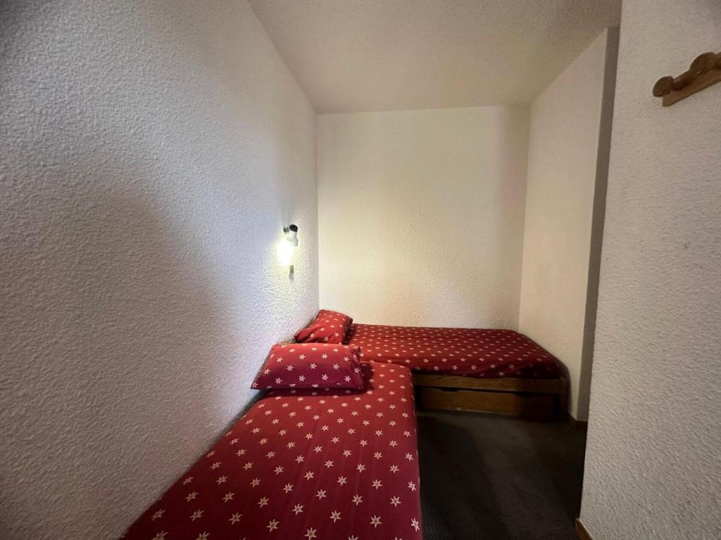 Cette petite chambre comprend un petit lit avec des draps rouges. dans l'établissement Residence 3000 Bail - Studio pour 4 Personnes 31, à Mâcot La Plagne