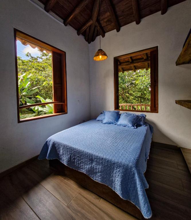 a bedroom with a bed with a blue comforter and two windows at Caminos Alojamiento in Jardin