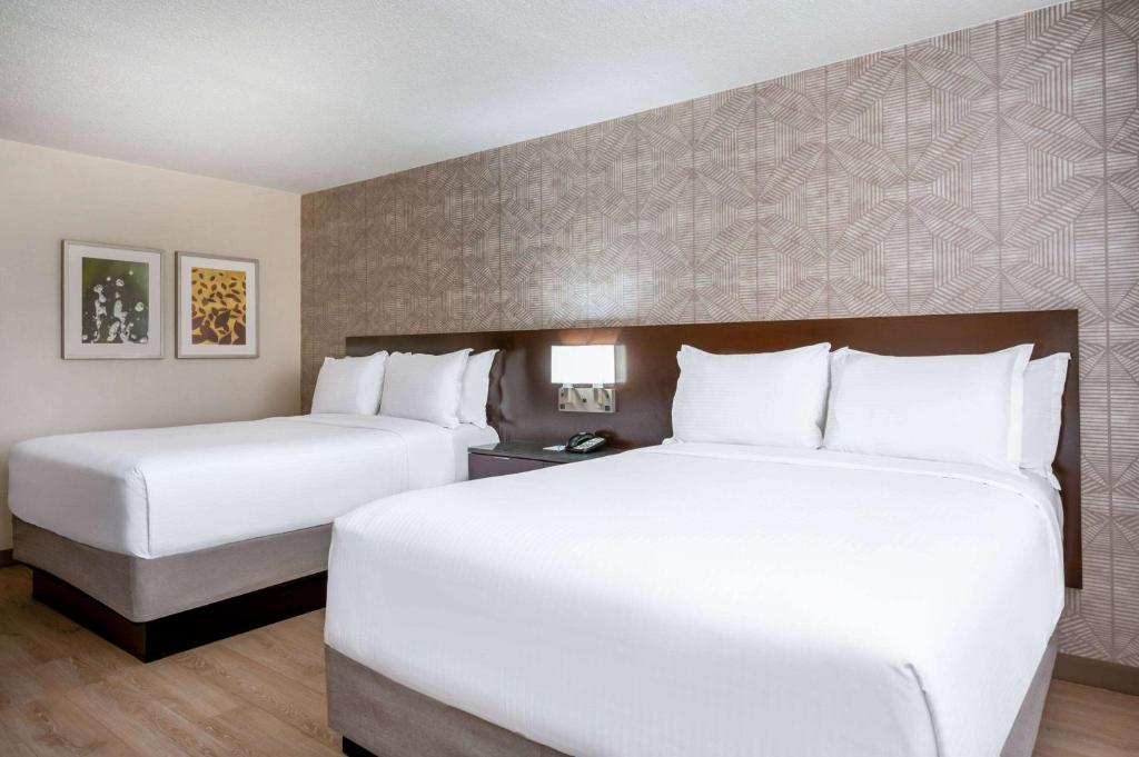 two beds in a hotel room with white sheets at Wyndham Indianapolis Airport in Indianapolis
