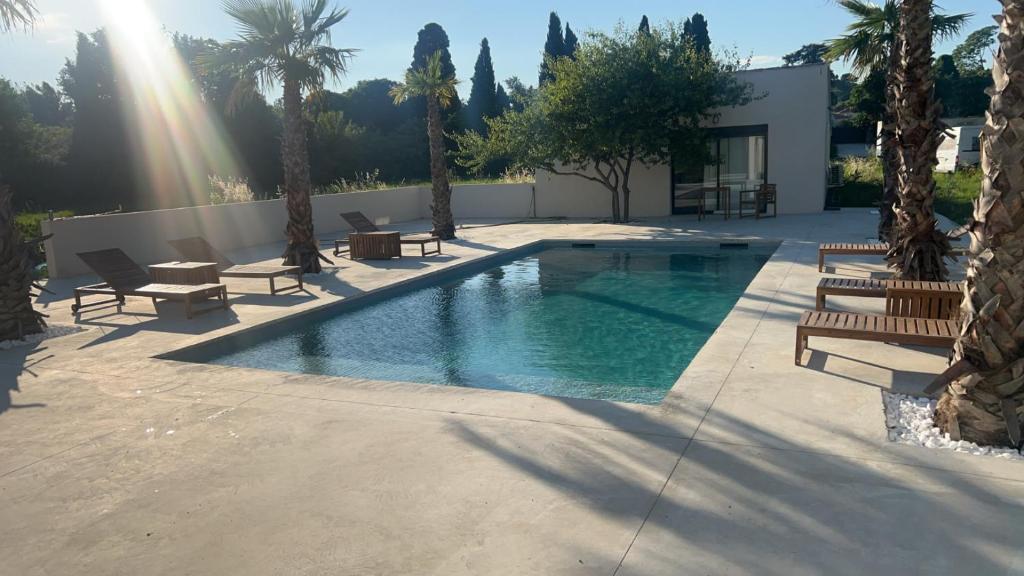 une piscine avec des bancs et des palmiers à côté d'un bâtiment dans l'établissement La suite iris, à Nîmes