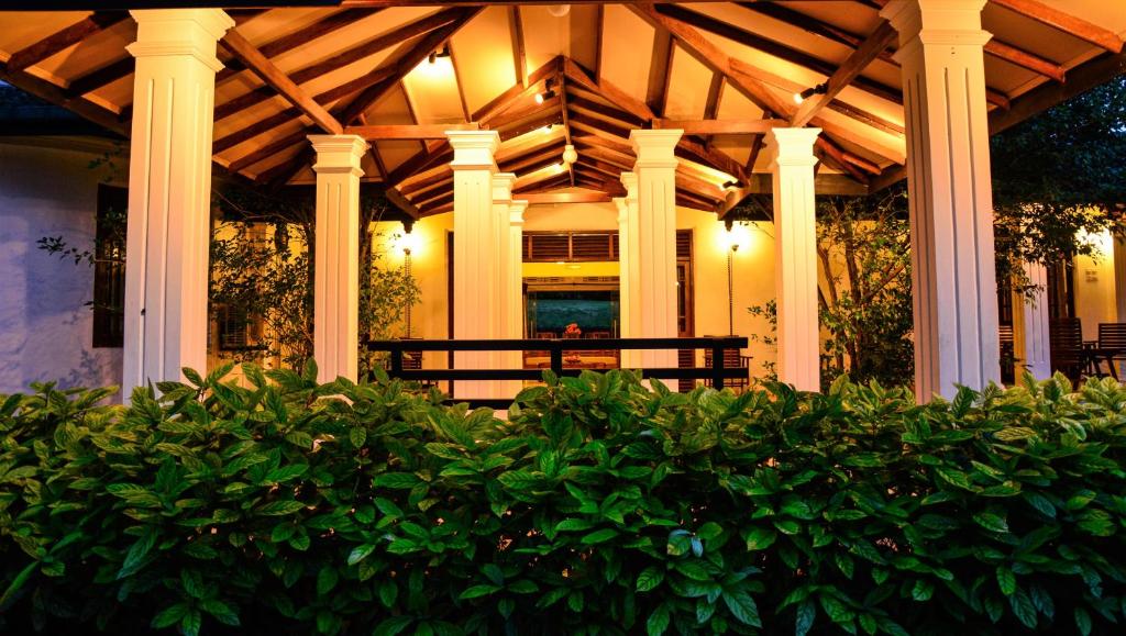 a house with a porch with columns and bushes at Camellia Dwelling in Hikkaduwa