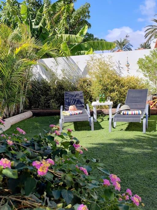 two chairs and a table in a yard with flowers at Oasis Los Porches in Playa del Ingles