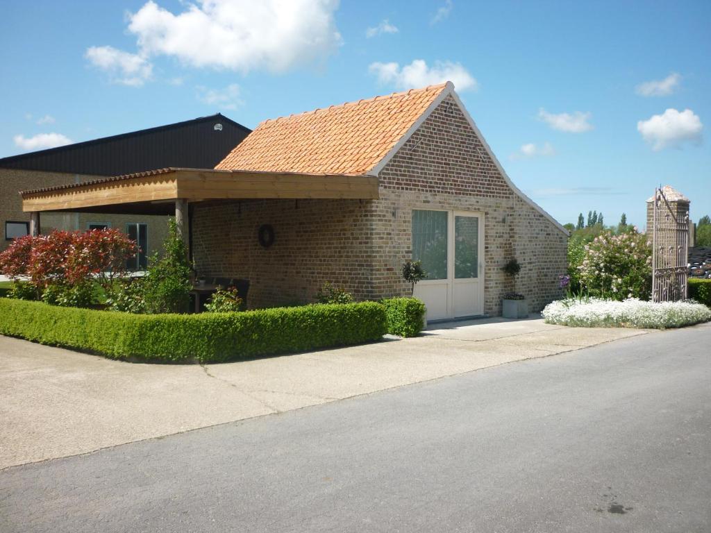 uma pequena casa de tijolos com uma porta branca em Hoveke Paddebroek em Alveringem