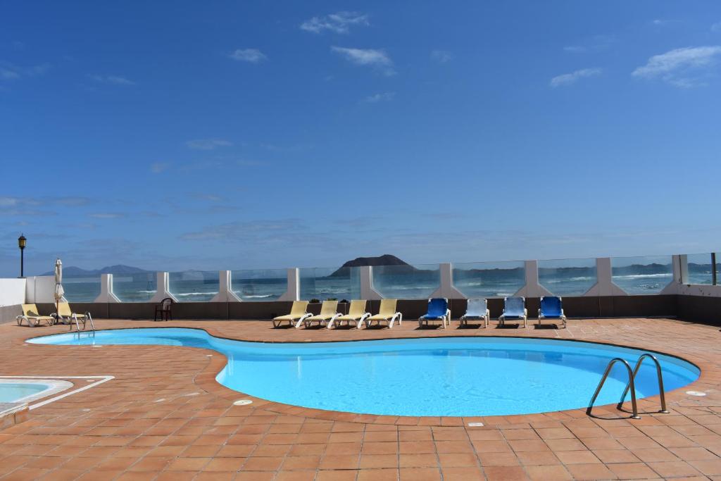 a swimming pool with chairs and the ocean in the background at Almina in Corralejo