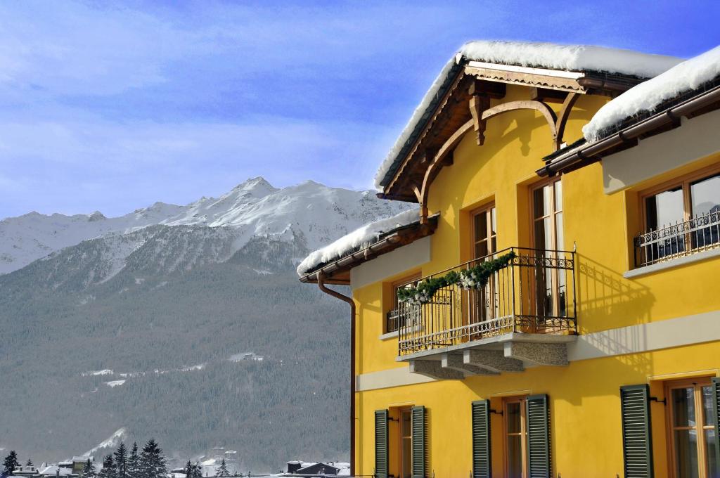 a yellow building with a snow covered mountain in the background at Hotel Meublè Sertorelli Reit in Bormio