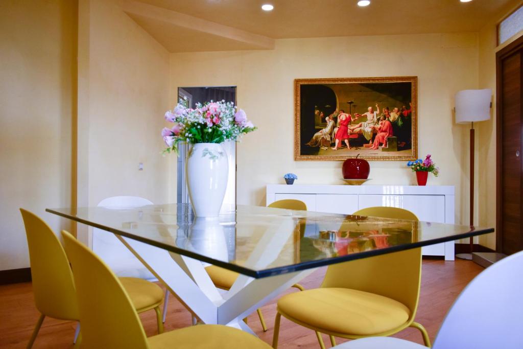 Una mesa de cristal con sillas amarillas y un jarrón con flores. en Domus DiDio, en Roma