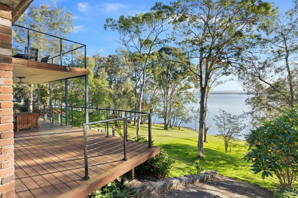 a house with a deck with a view of the water at Waterfront Treetops Getaway in Wangi Wangi