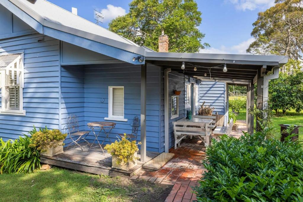 ein blaues Haus mit einer Veranda mit einer Bank in der Unterkunft Meroo Meadow Magic Charming Cottage Retreat in Meroo