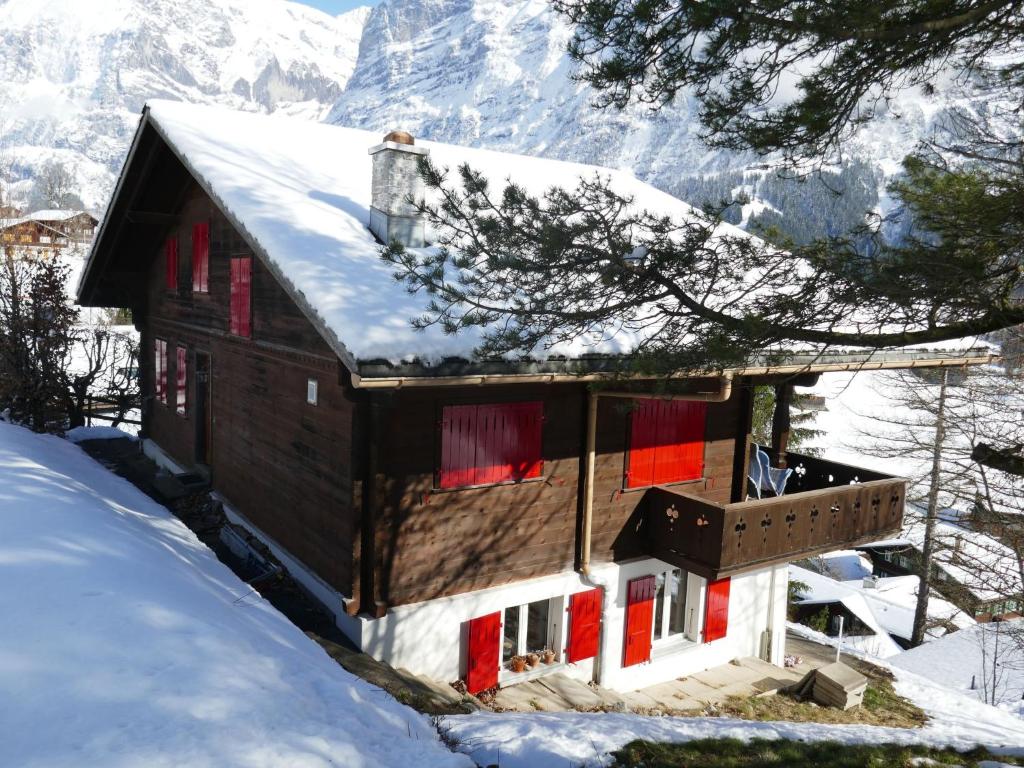 una casa cubierta de nieve con montañas en el fondo en Apartment Chalet Colette-1 by Interhome, en Grindelwald