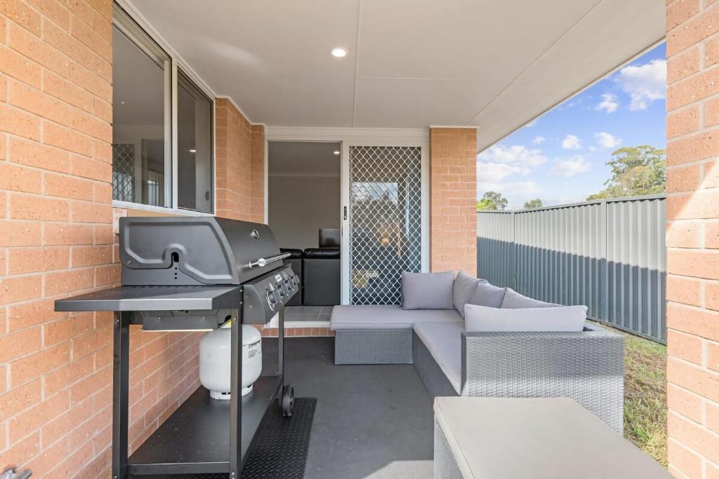 een terras buiten met een barbecue en een bank bij Hunter Explorer - Games Room & Outdoor Spa in Cessnock