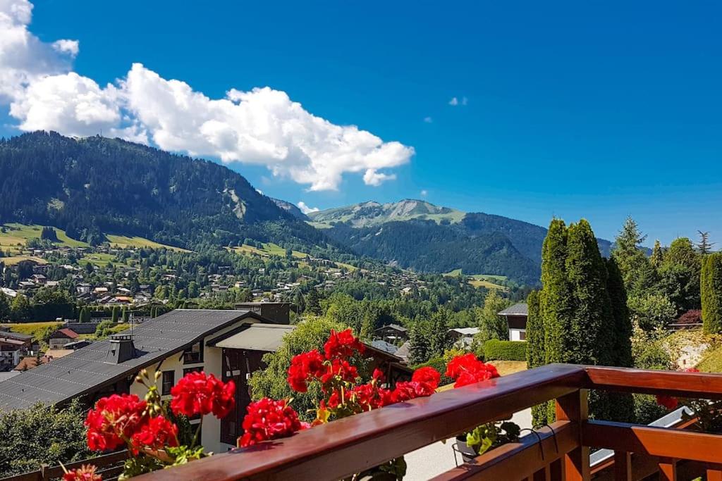 d'un balcon avec des fleurs rouges et des montagnes en arrière-plan. dans l'établissement Exceptional view of village and mountain, à Megève