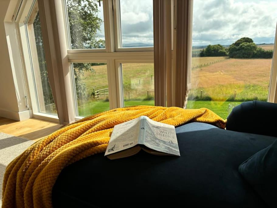 a bed with a blanket and a newspaper on it with a window at Thistledown Lodge - Devon in North Tawton