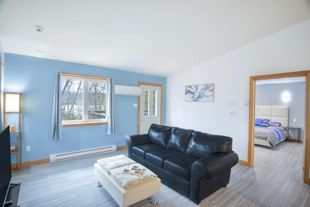 a living room with a black leather couch and a bed at Tucked Away Walk to Beach Pet Friendly Relax in Rothesay