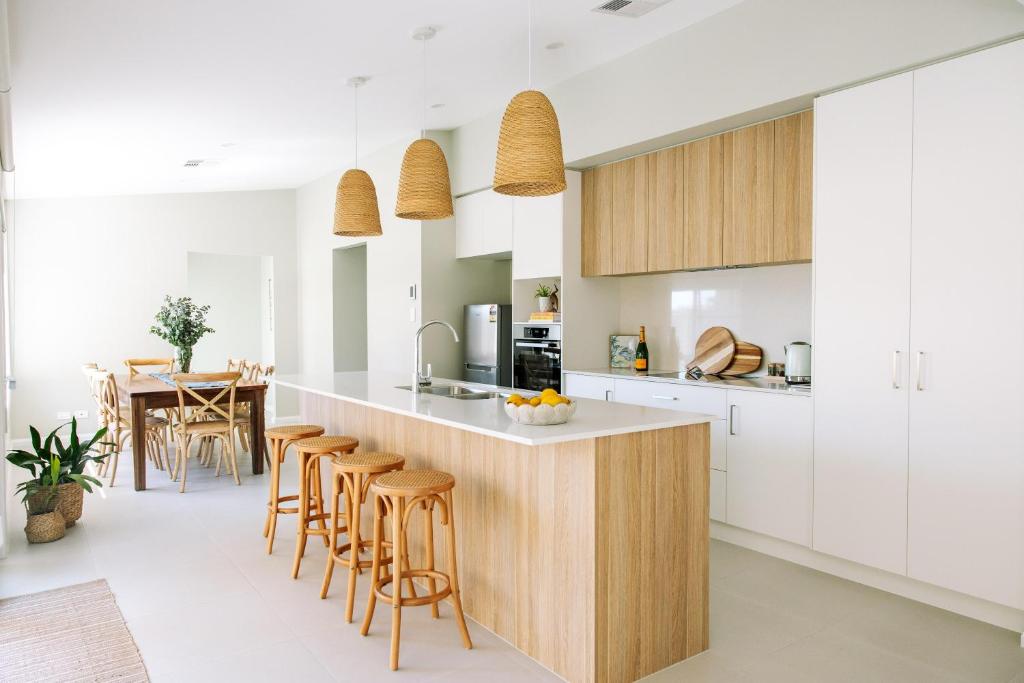 cocina con armarios blancos y barra con taburetes en House of Banksia, en Long Jetty