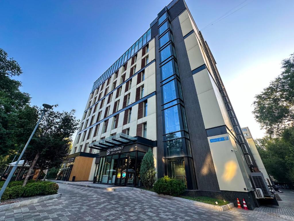 a tall building with glass windows on a street at Resident City Hotel in Almaty