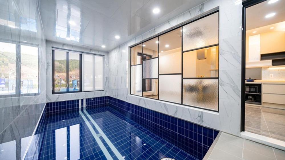 a swimming pool with blue tiles in a room with windows at Gapyeong Casabella Pool Villa in Mak-kol