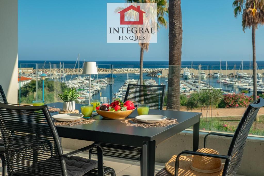 a table with a bowl of fruit on a balcony with a harbor at Apartament Mar Blau in Palamós