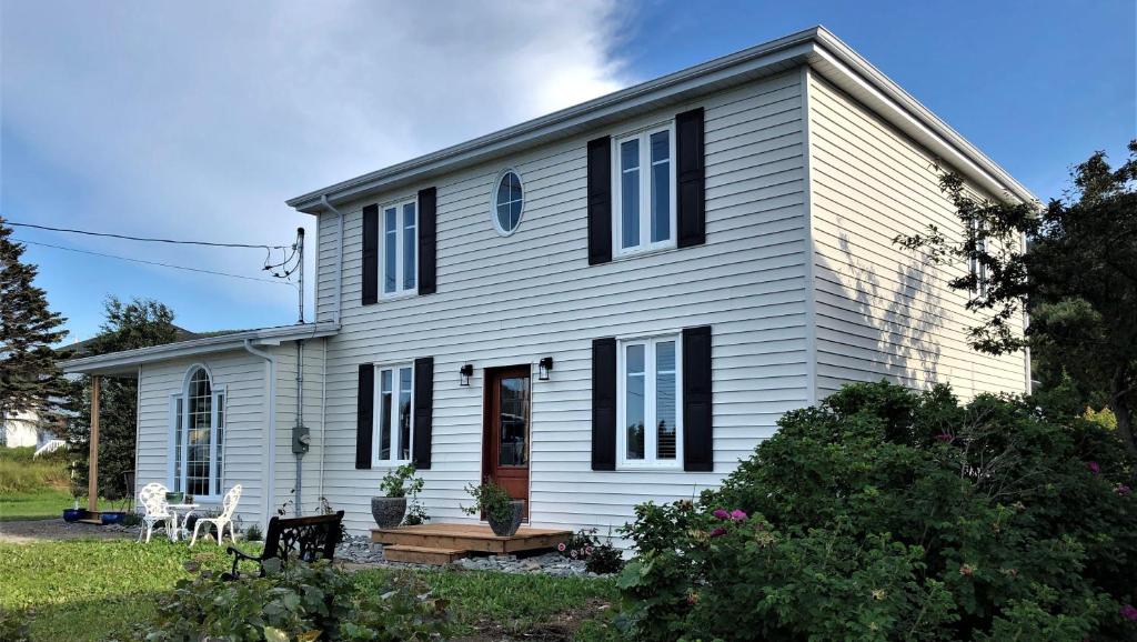 a white house with black windows and a yard at Auberge Évasion Nature Petite-Vallée in Petite-Vallée