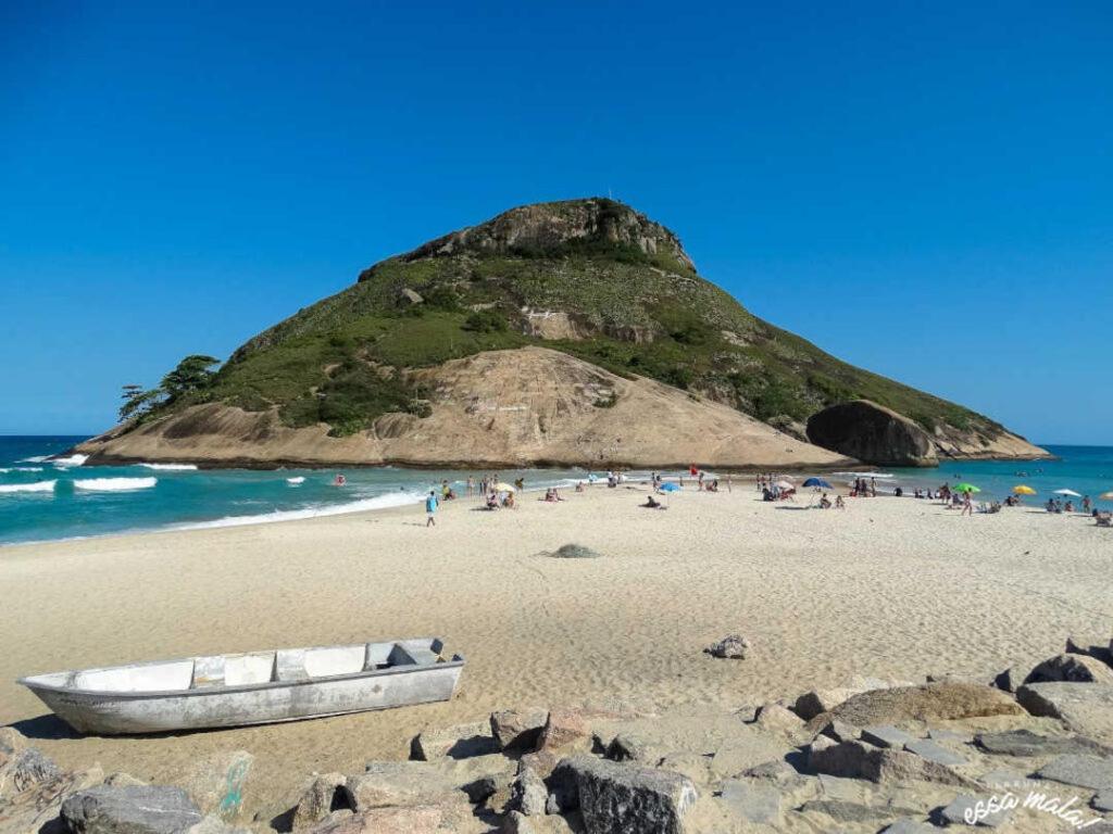 Un barco en una playa con una colina al fondo en Apartamento aconchegante no Recreio, en Río de Janeiro