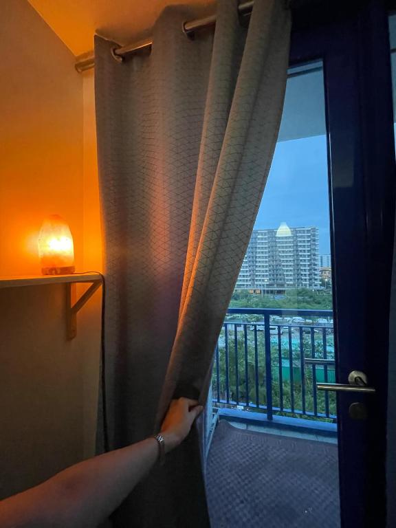 a person opening a curtain in a room with a balcony at Moa Sea Residences Staycation in Manila