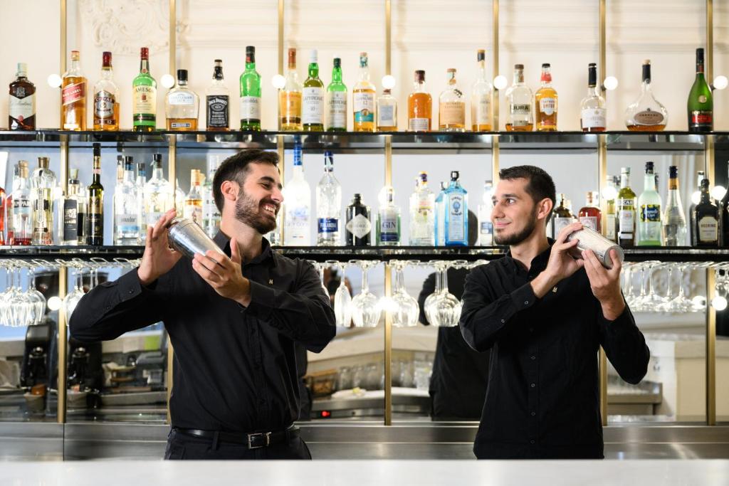 two men standing in a bar holding up glasses at Nemzeti Hotel Budapest - MGallery Collection in Budapest