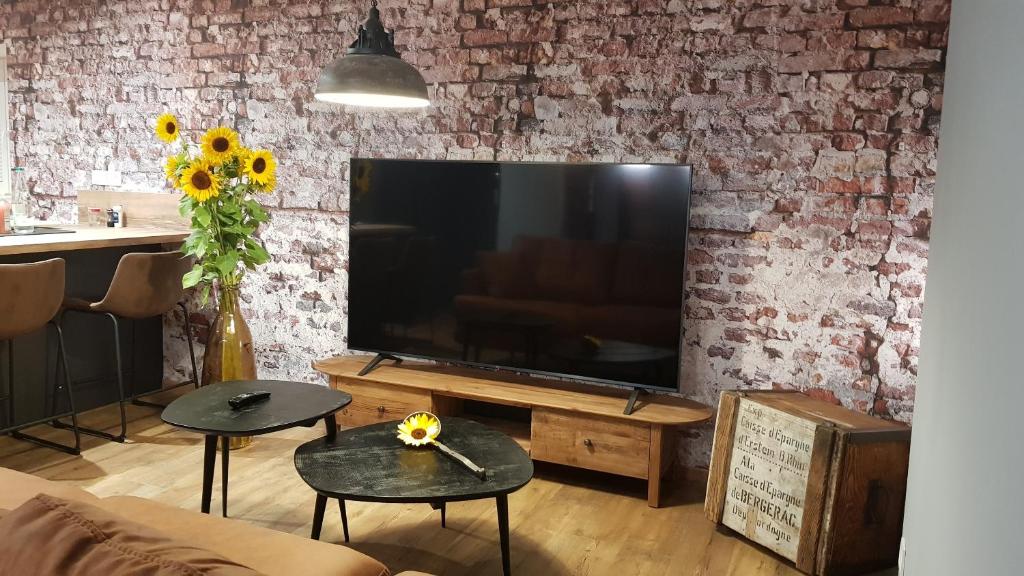 a living room with a large television on a brick wall at L'ESCALE d'ALSACE in Lièpvre