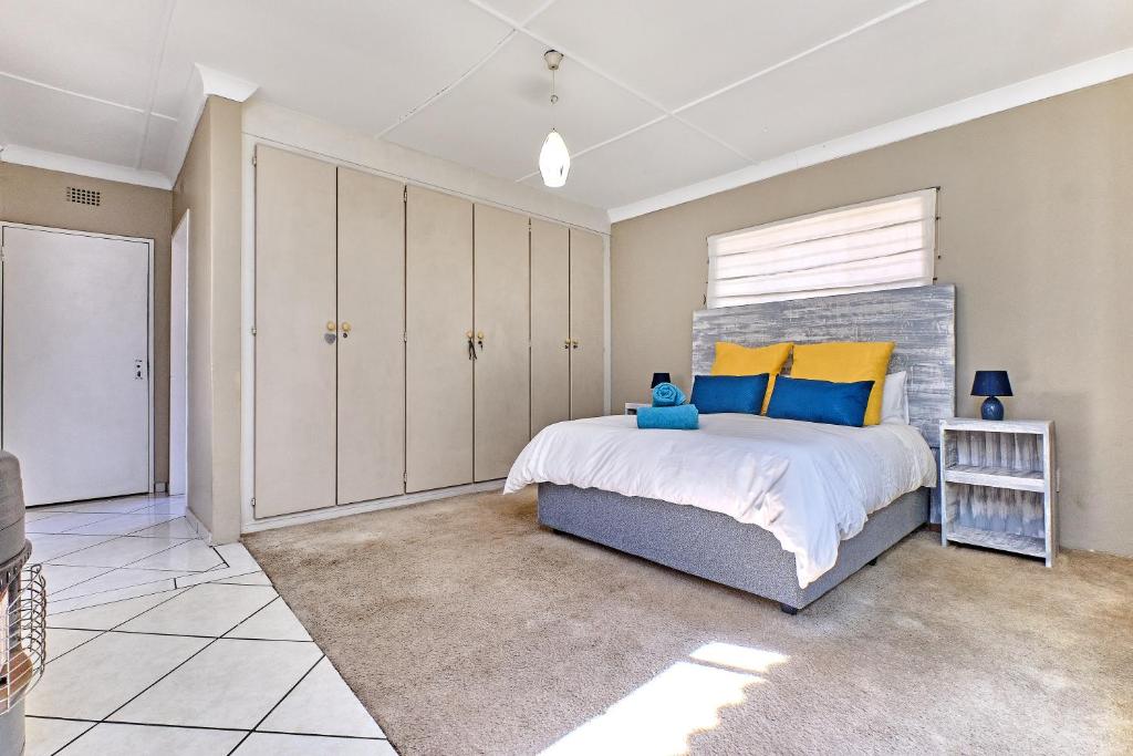 a bedroom with a large bed with yellow and blue pillows at Tranquil, large 1 bedroom garden cottage, 12 mins from OR Tambo International with backup water in Germiston