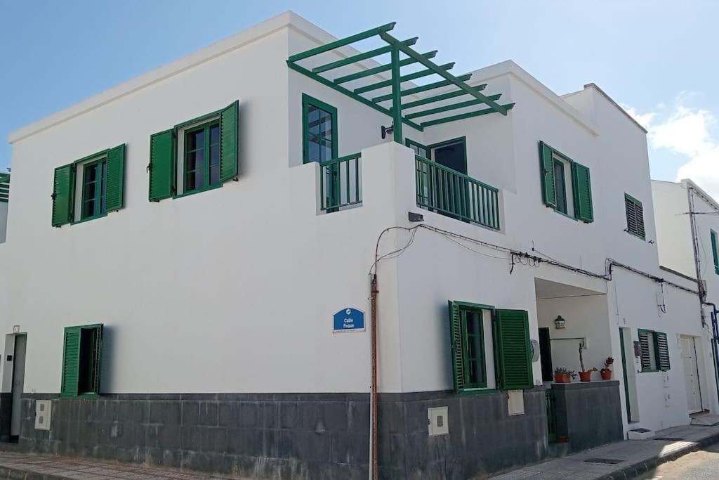 a white building with green shuttered windows on a street at famarabeach2 in Famara