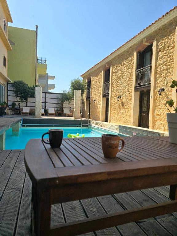 two cups on a wooden table next to a pool at Volakas Beachfront Suites in Rethymno