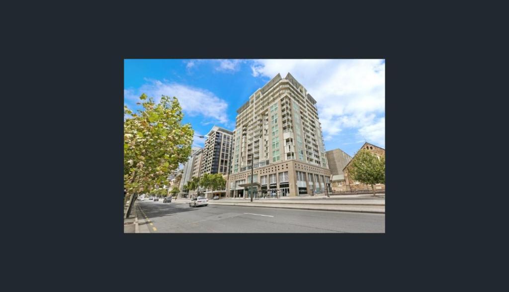 un edificio alto en una calle de la ciudad con un árbol en Happy BNB deluxe suit in adelaide CBD, en Adelaida