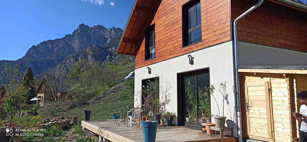 a house with a wooden deck with mountains in the background at Joli studio à la montagne studio à la montagne in Les Vigneaux